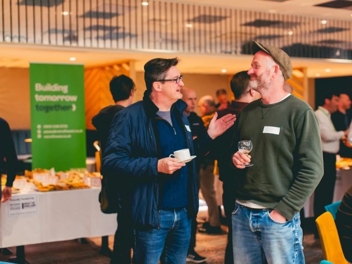 Two middle ages men chatting. Behind them is a stall with a green banner
