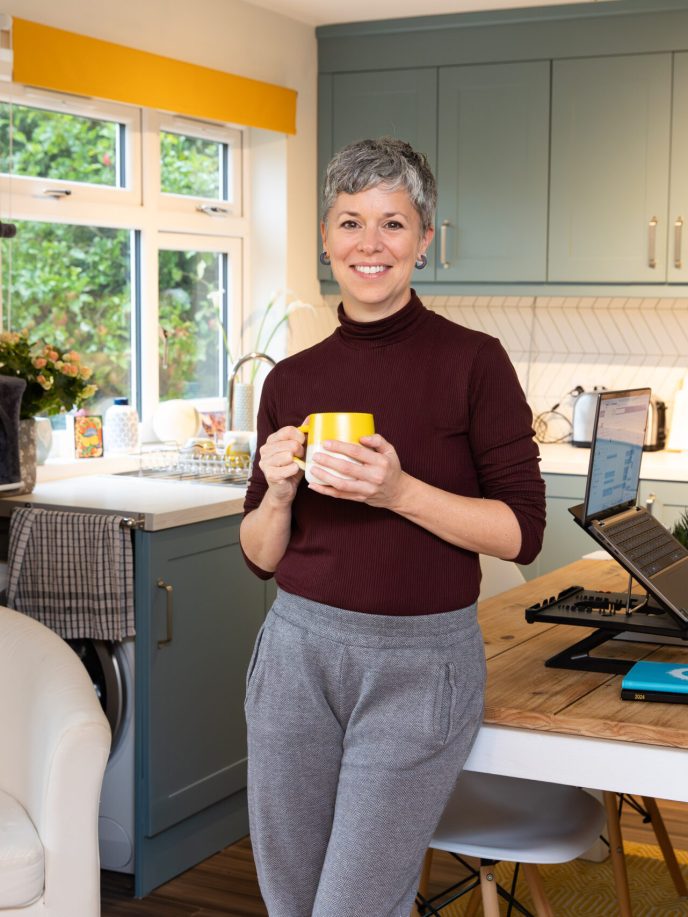 Smiling woman holding a hot drink in front of her light, clean kitchen